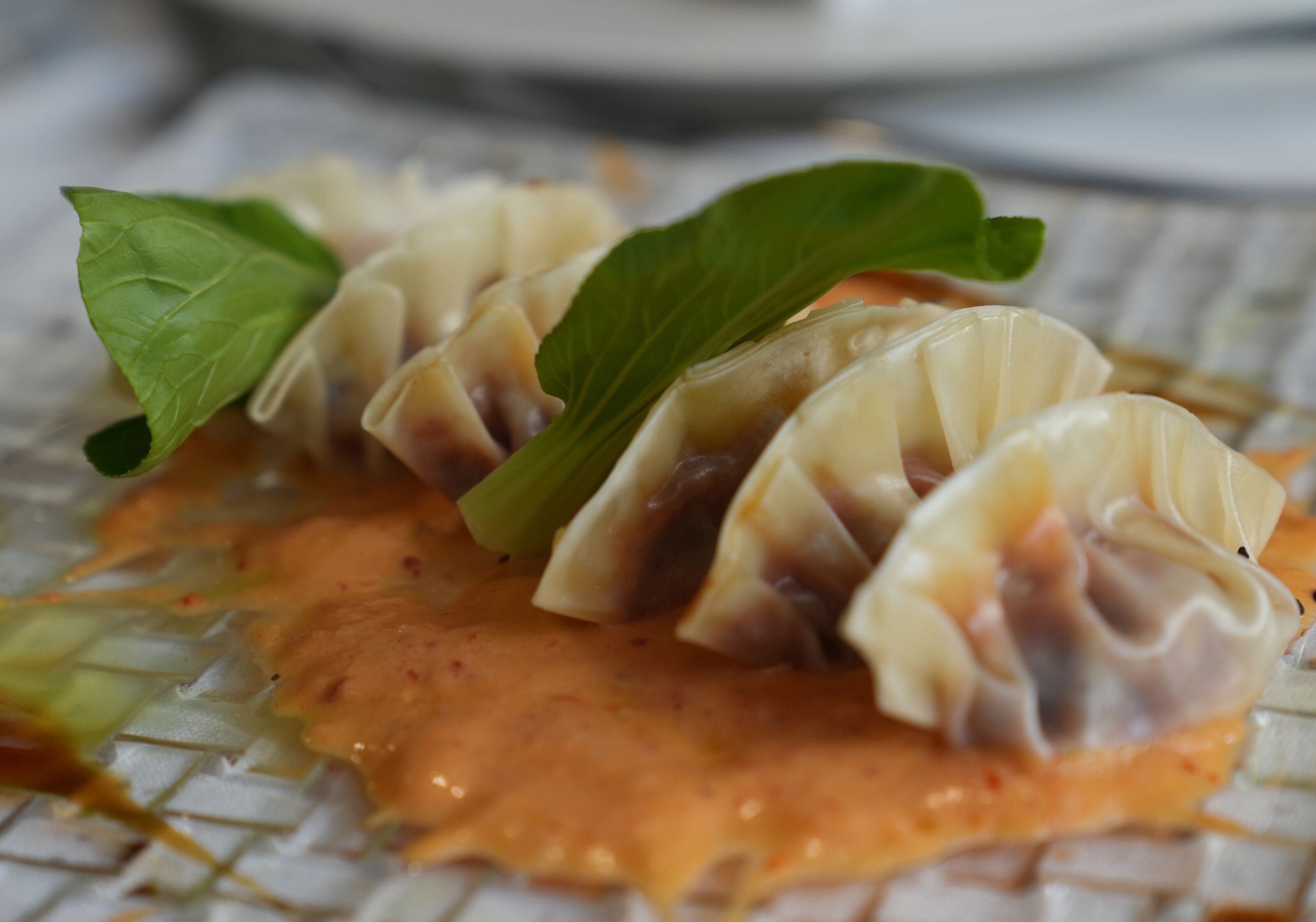 Un plato de dumplings con salsa y hojas de albahaca.