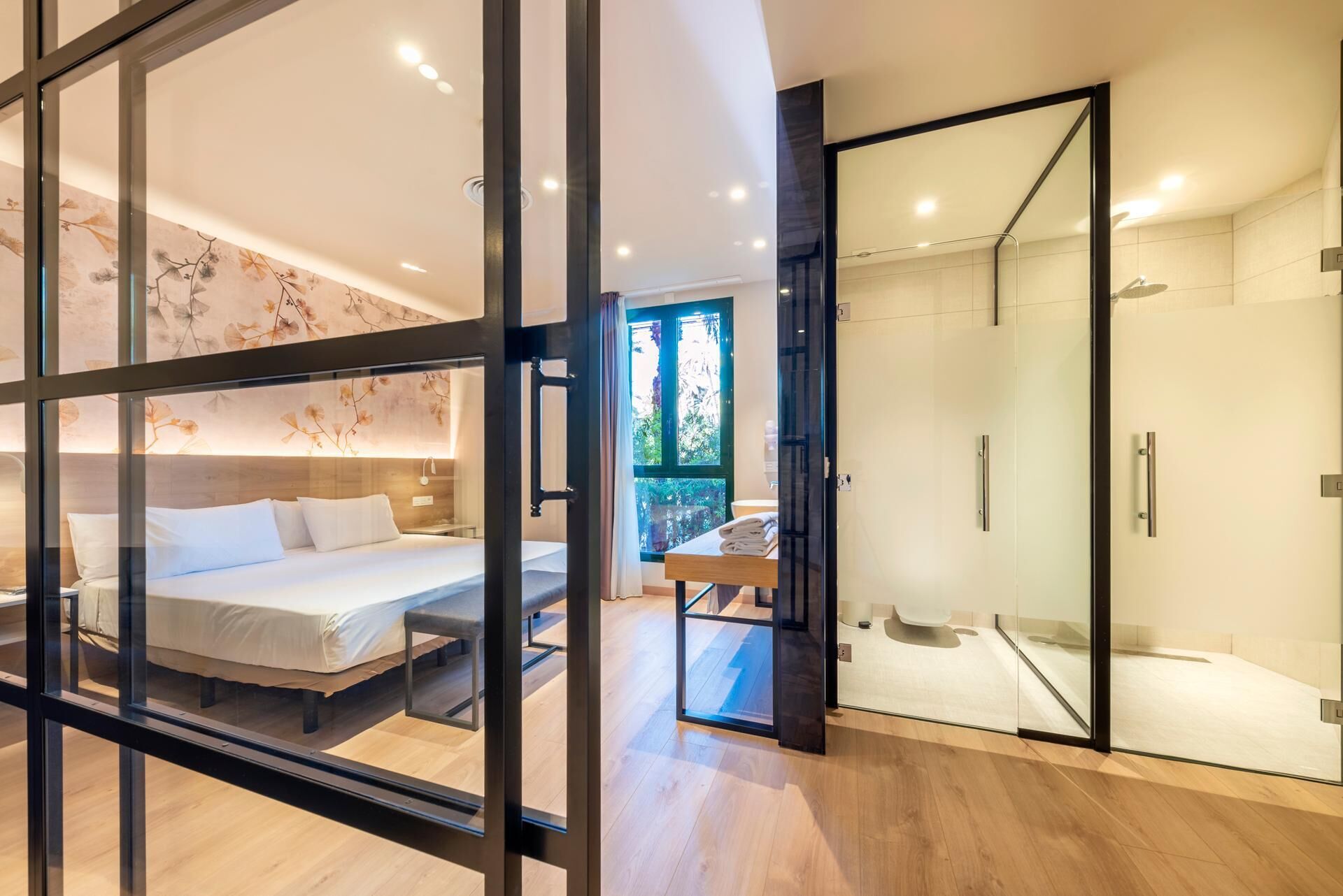 Una habitación de hotel moderna con cama, cabina de ducha de vidrio y vistas a zonas verdes.