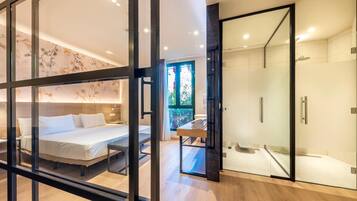 Una habitación de hotel moderna con cama, cabina de ducha de vidrio y vistas a zonas verdes.