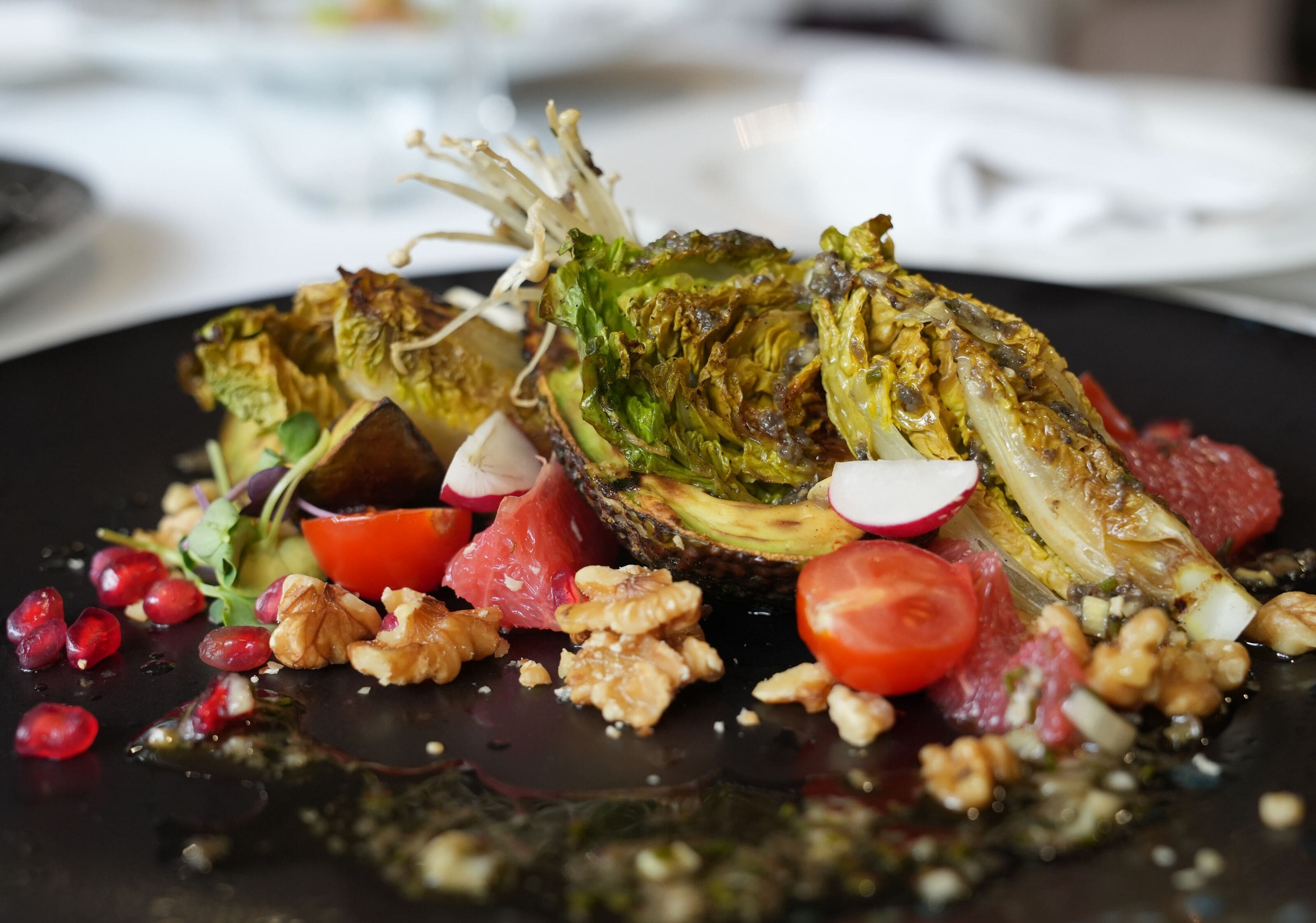 Un plato con verduras asadas, nueces y rábanos sobre un fondo oscuro.