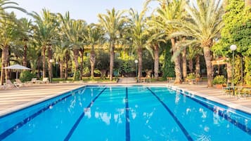 Una piscina con agua azul cristalina, rodeada de palmeras y sillas de descanso.