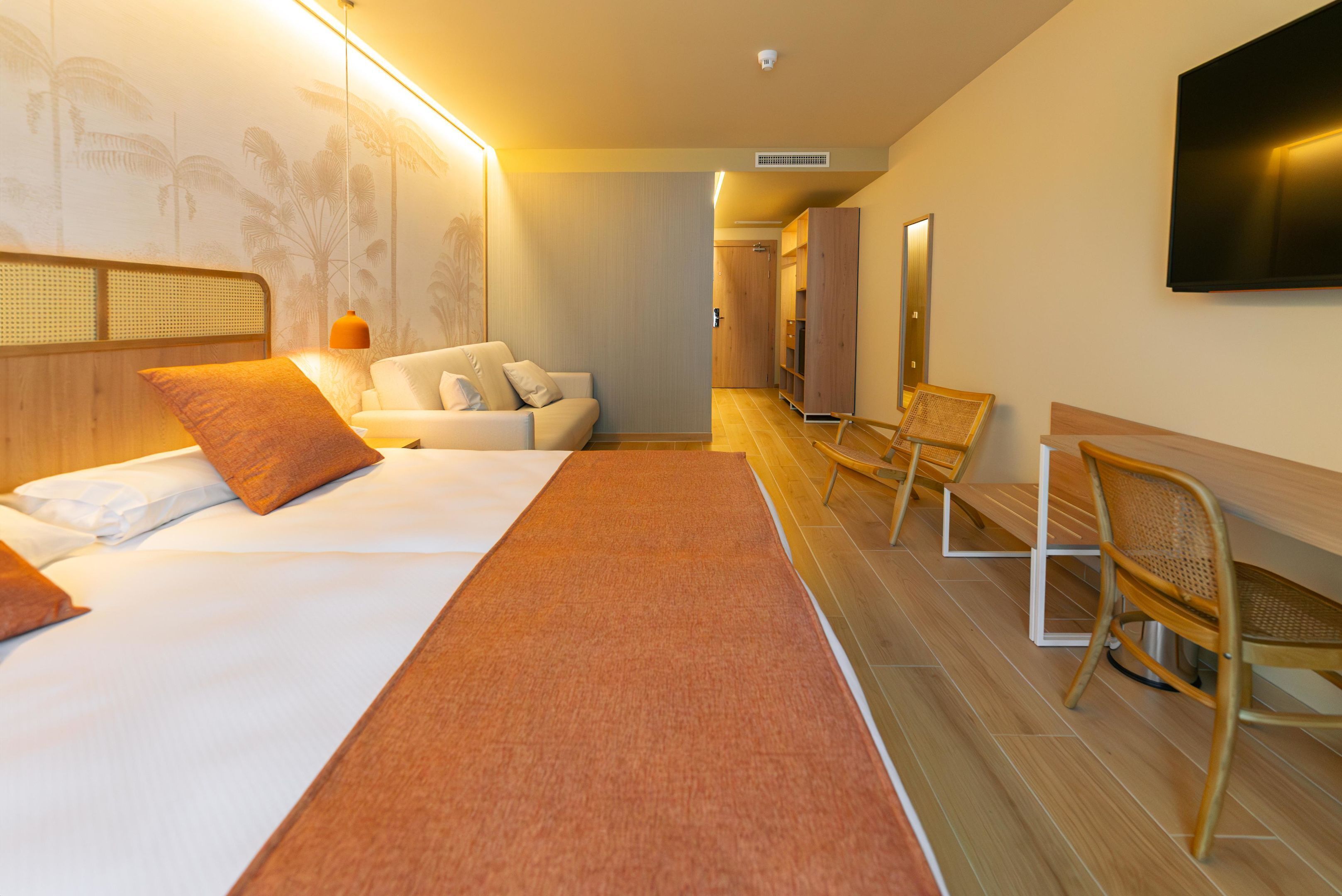 A hotel room with a bed, a sofa, a desk, and a TV.