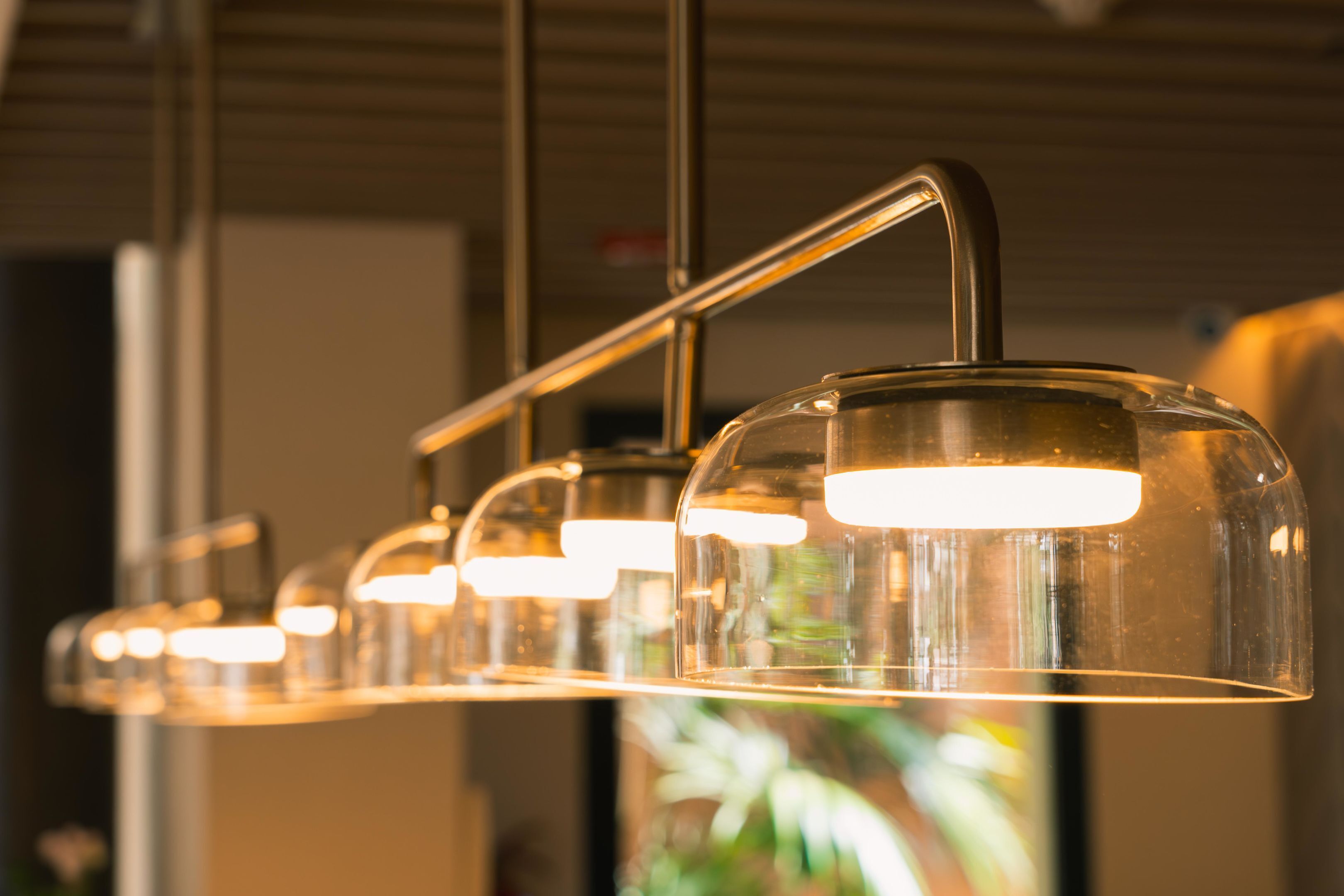 A row of pendant lights with a metallic finish and clear glass shades, hanging from a ceiling with a visible structural beam.