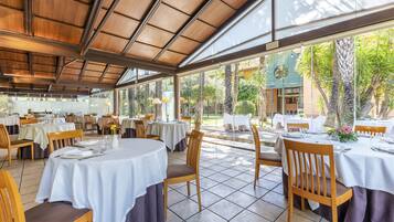 Un restaurante con mesas redondas, sillas de madera y un patio cubierto con paredes de vidrio.