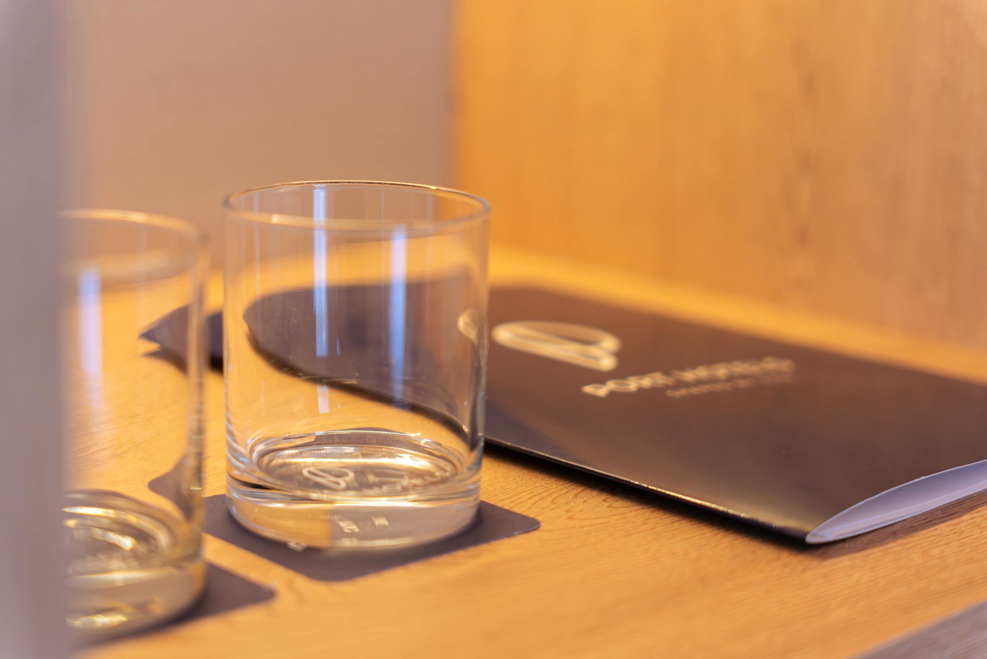 Una computadora portátil sobre una superficie de madera, con dos vasos transparentes a su lado.