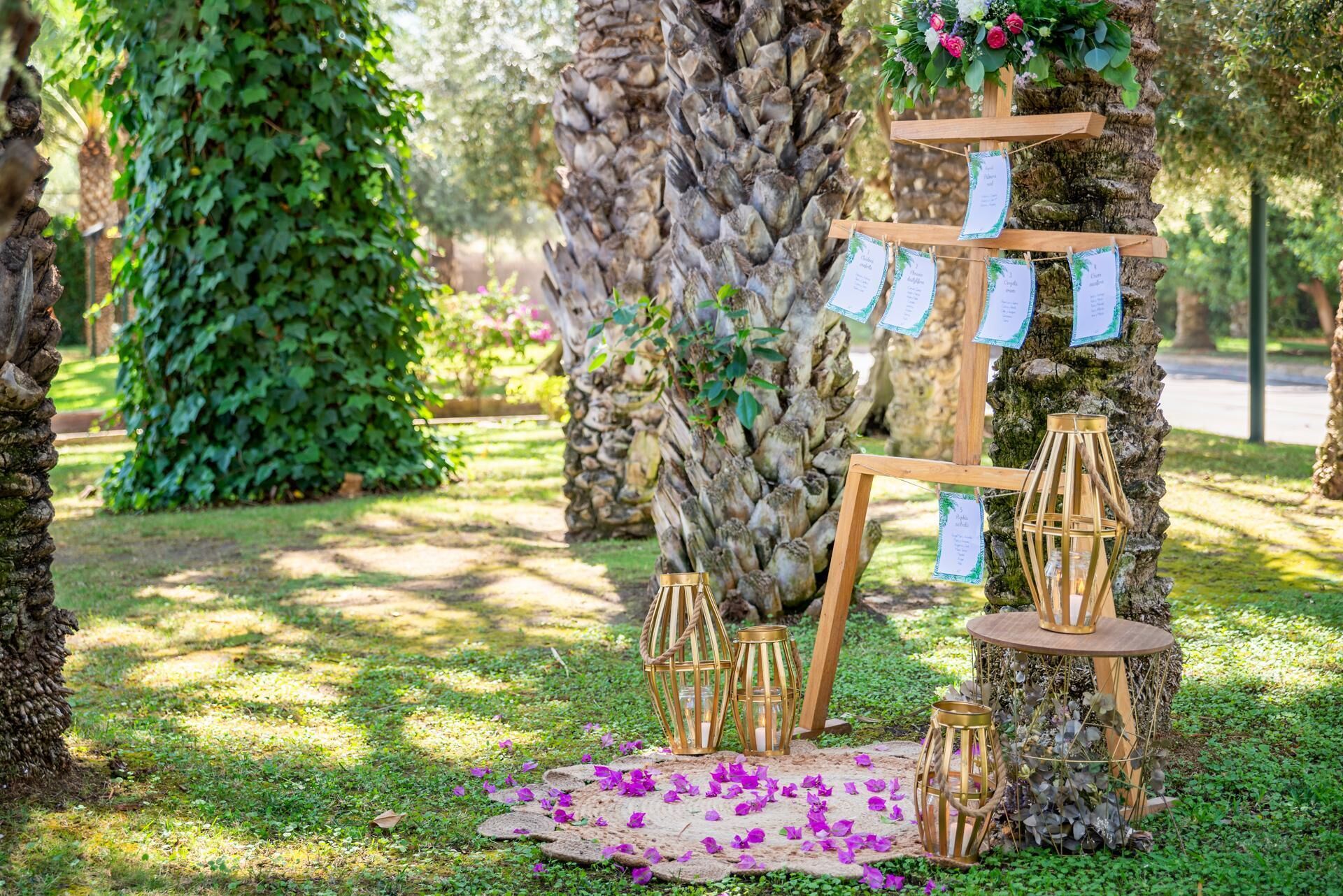 Et rustikt udendørs bryllupsarrangement med en træport, lanterner og blomsterdekorationer.
