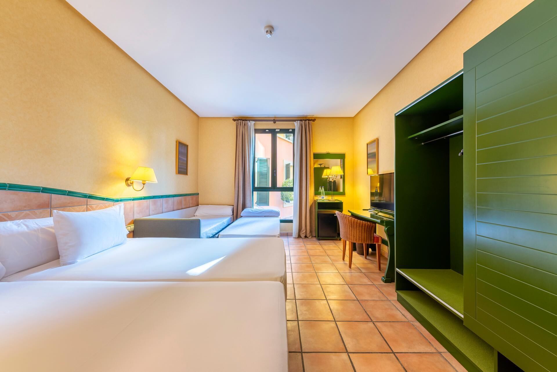 A hotel room with two beds, a desk, a chair, a TV, and a green wall.