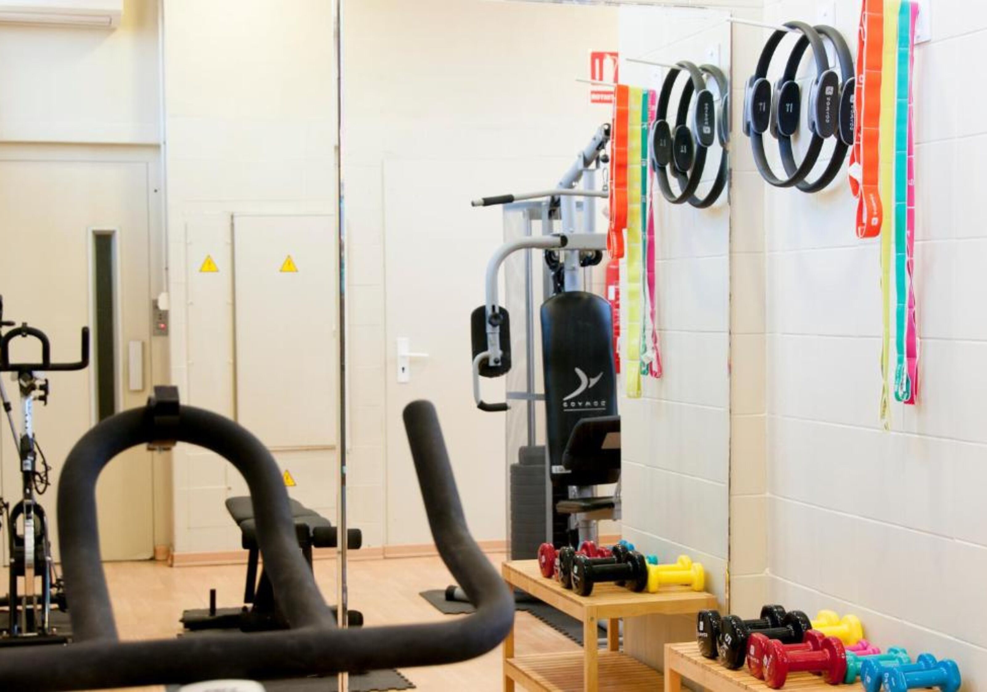 Un gimnasio con equipo de ejercicio, incluyendo una máquina de remo, un banco de pesas y varias mancuernas.
