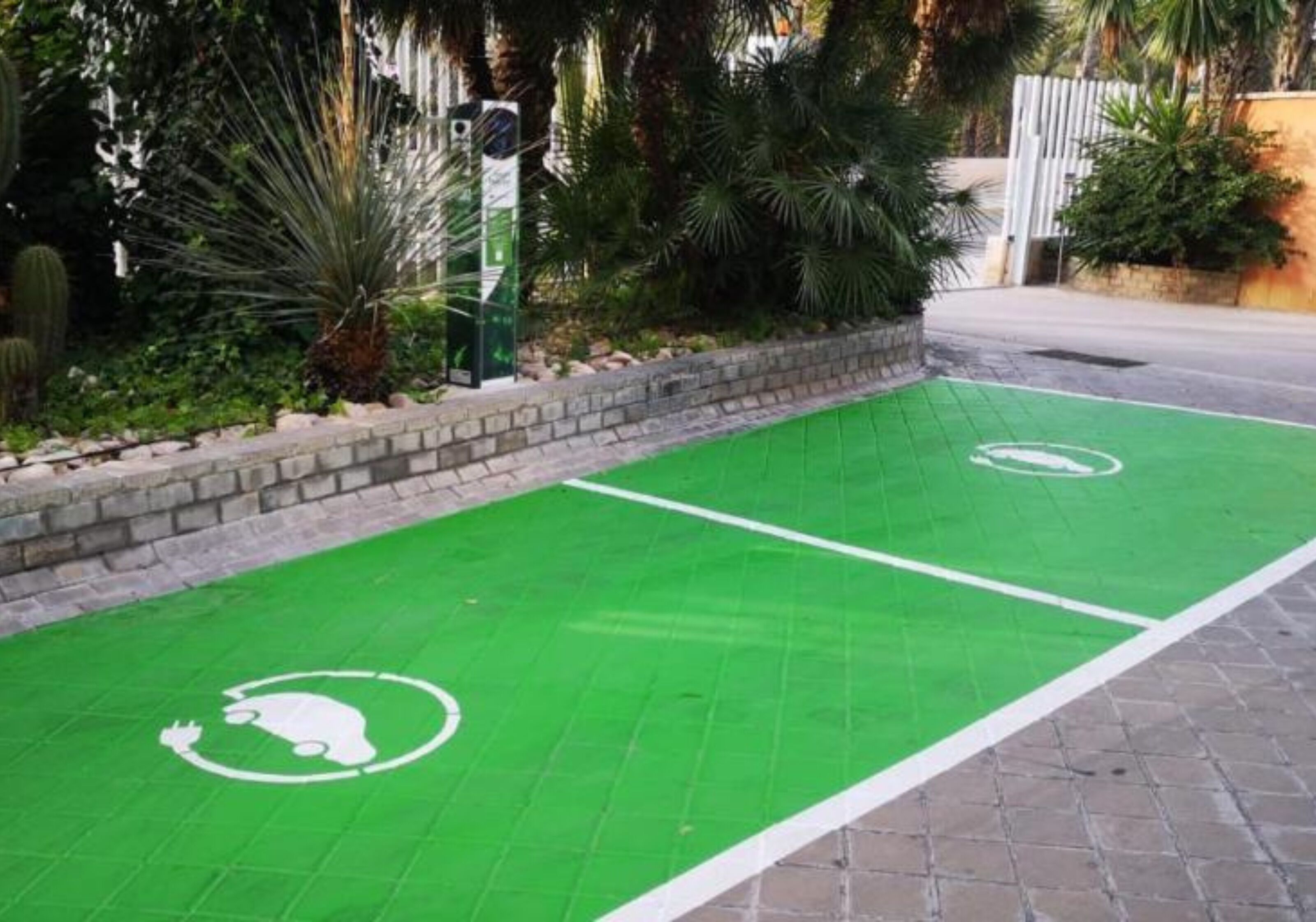 A green parking area with a white parking symbol, surrounded by a stone wall and lush greenery.