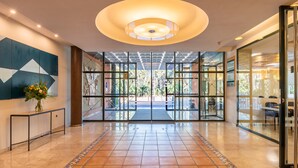 Un vestíbulo amplio con suelo de baldosas, una lámpara central y vistas a un área exterior a través de puertas de cristal.