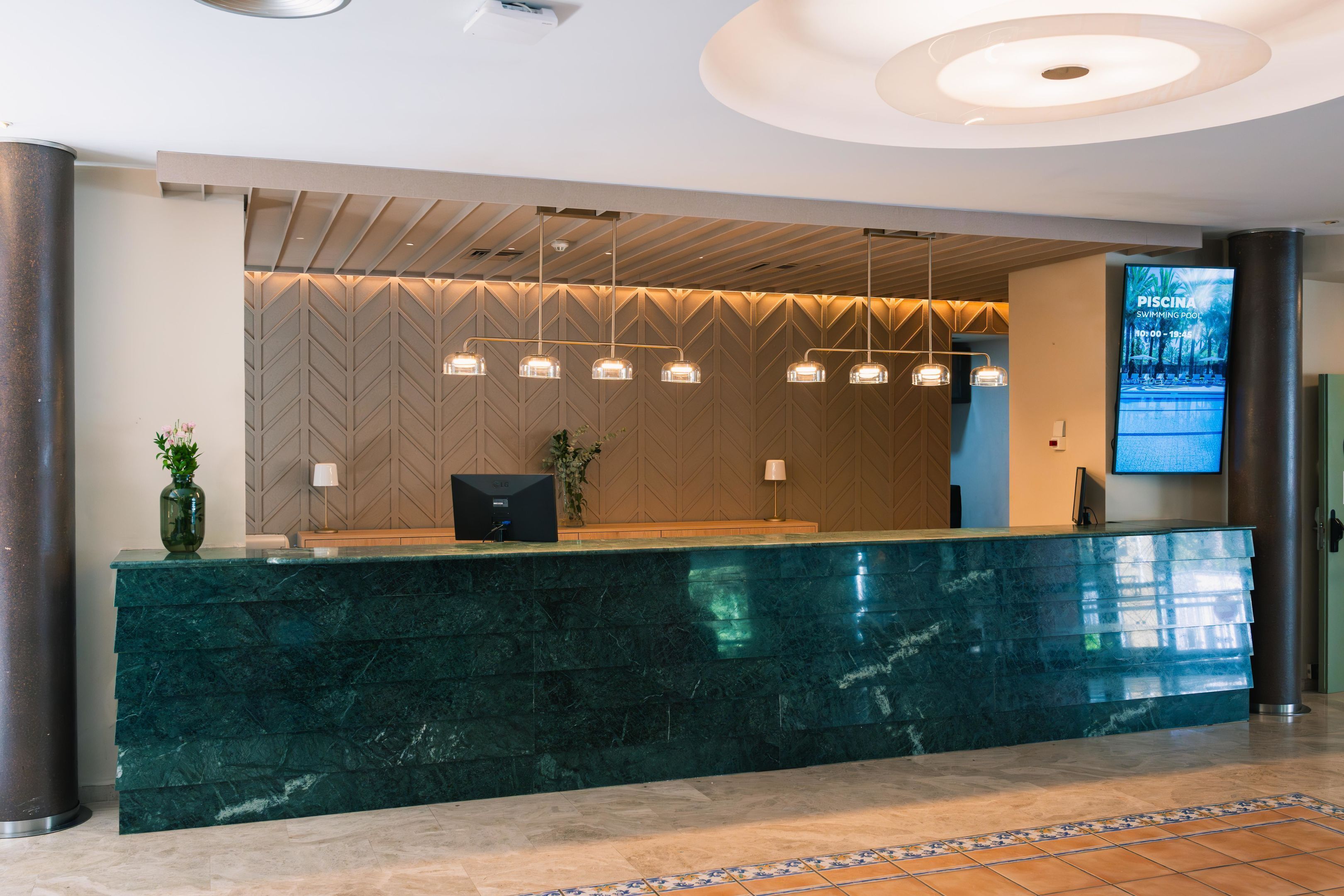 A reception desk with a green marble top, a wooden panel wall, and pendant lighting.