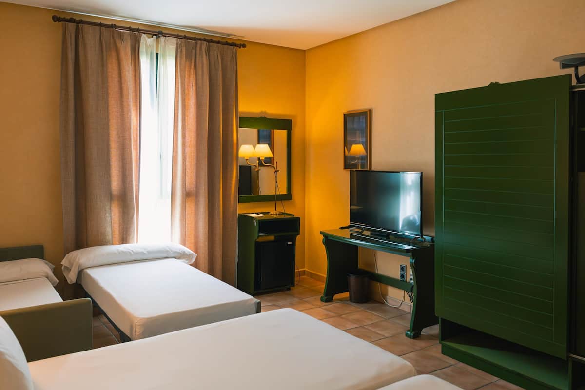 Ett hotellrum med två separata sängar, en tv, ett skrivbord med en lampa, en papperskorg och en grön garderob.