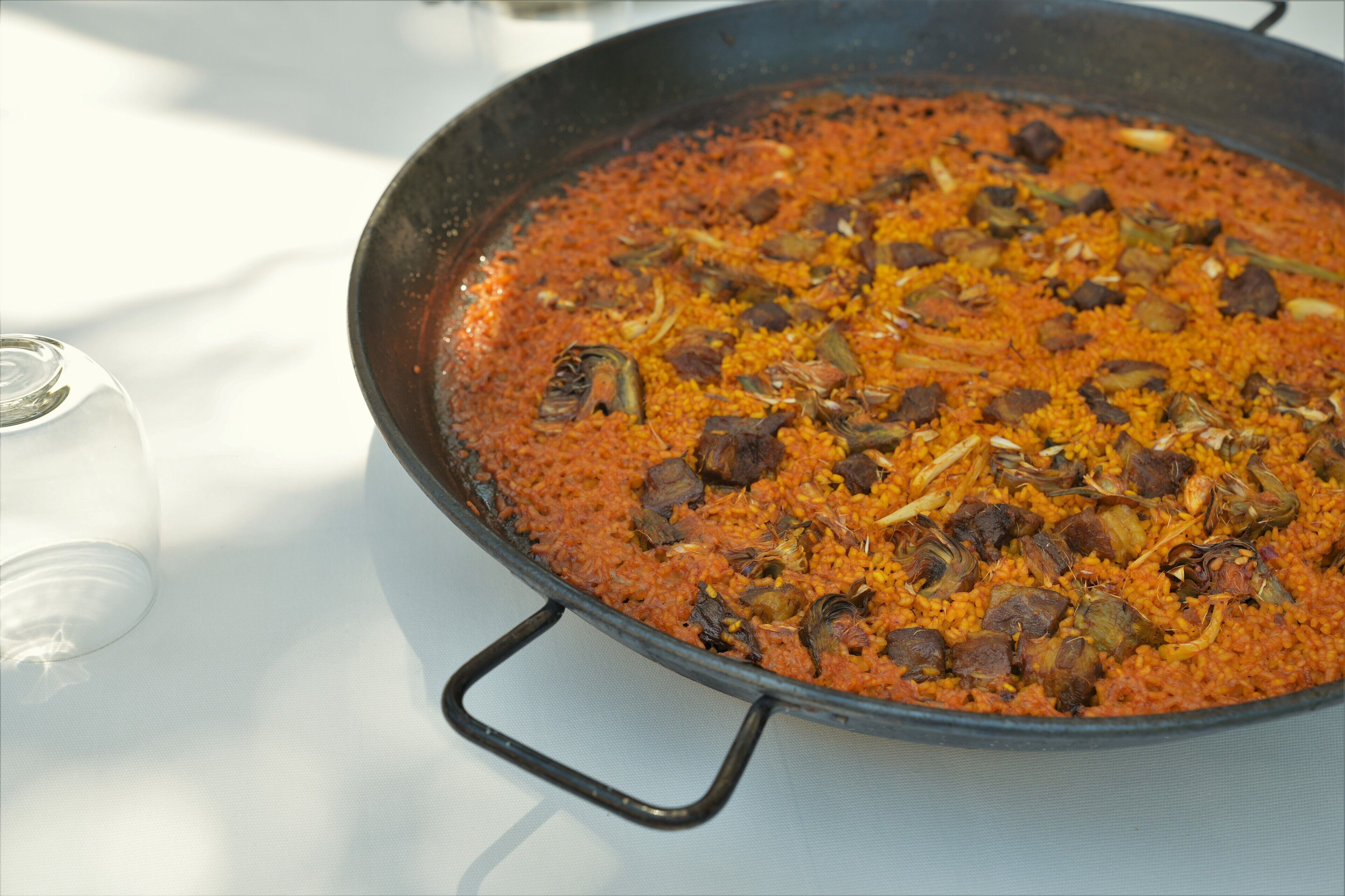 A large, shallow cooking pan filled with a red-colored dish, possibly a stew or curry, containing chunks of meat and vegetables.