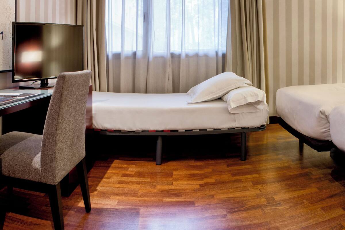 A hotel room with a desk, two beds, a chair, and a TV.