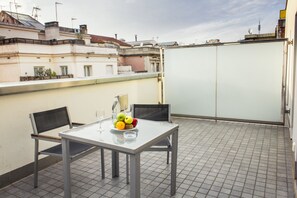 Terraza en la azotea con una mesa para dos, un frutero y un vaso de agua.