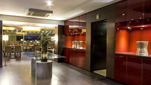Un moderno vestíbulo de hotel con una mesa de vidrio central, decoración en rojo y negro, y un ascensor visible.