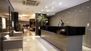 Un área de recepción de hotel moderna con un mostrador elegante, asientos cómodos y un amplio ventanal que ofrece vista al interior.
