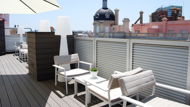 Una terraza en la azotea con mobiliario blanco, un paraguas grande y vistas a un edificio histórico con cúpula.