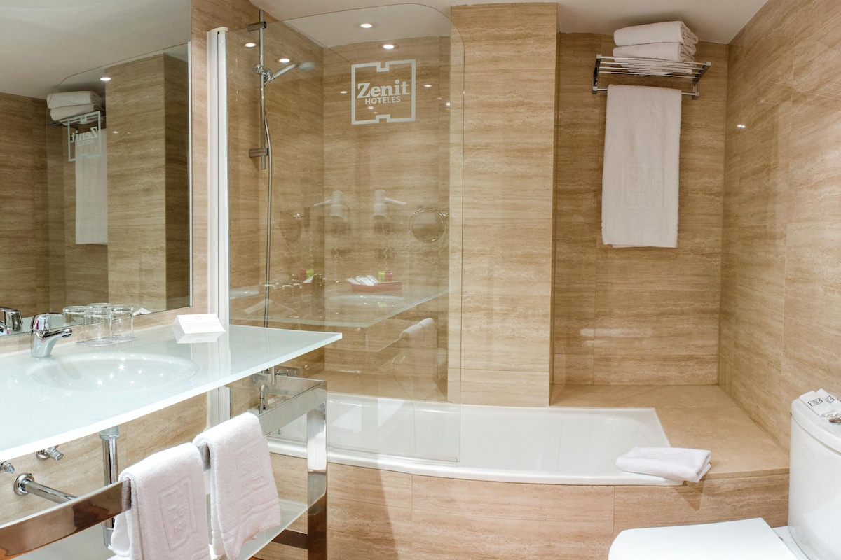 A modern bathroom with a glass-enclosed shower, a large bathtub, and a vanity with a mirror and sink.