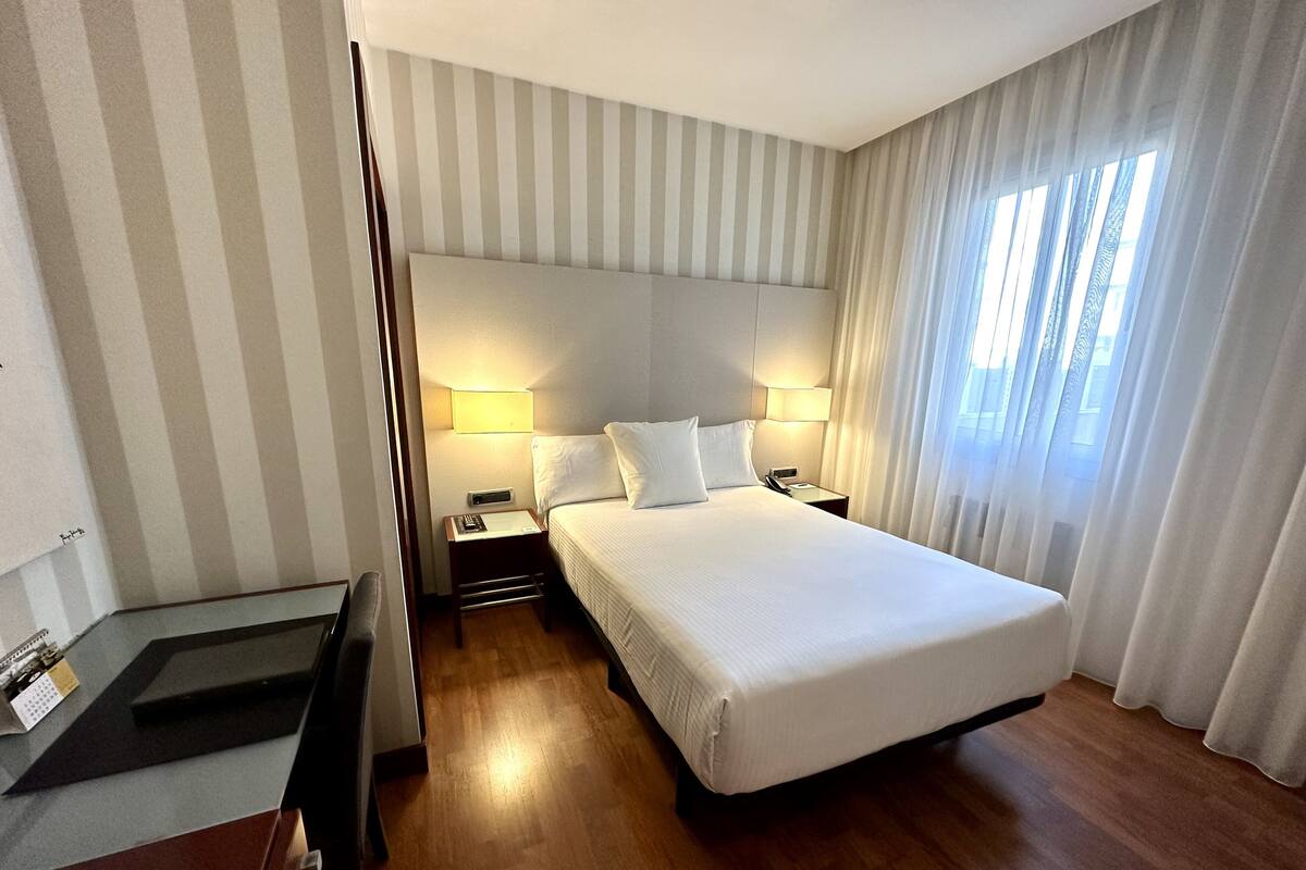 A hotel room with a large bed, two bedside tables, a desk, and a chair.