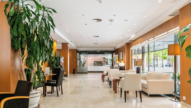 A hotel lobby with a reception desk, seating area, and large windows. - Sercotel de los Reyes (San Sebastian de los Reyes)