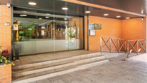 A hotel entrance with a glass door, steps leading up to it, and a brick wall. - Sercotel de los Reyes (San Sebastian de los Reyes)