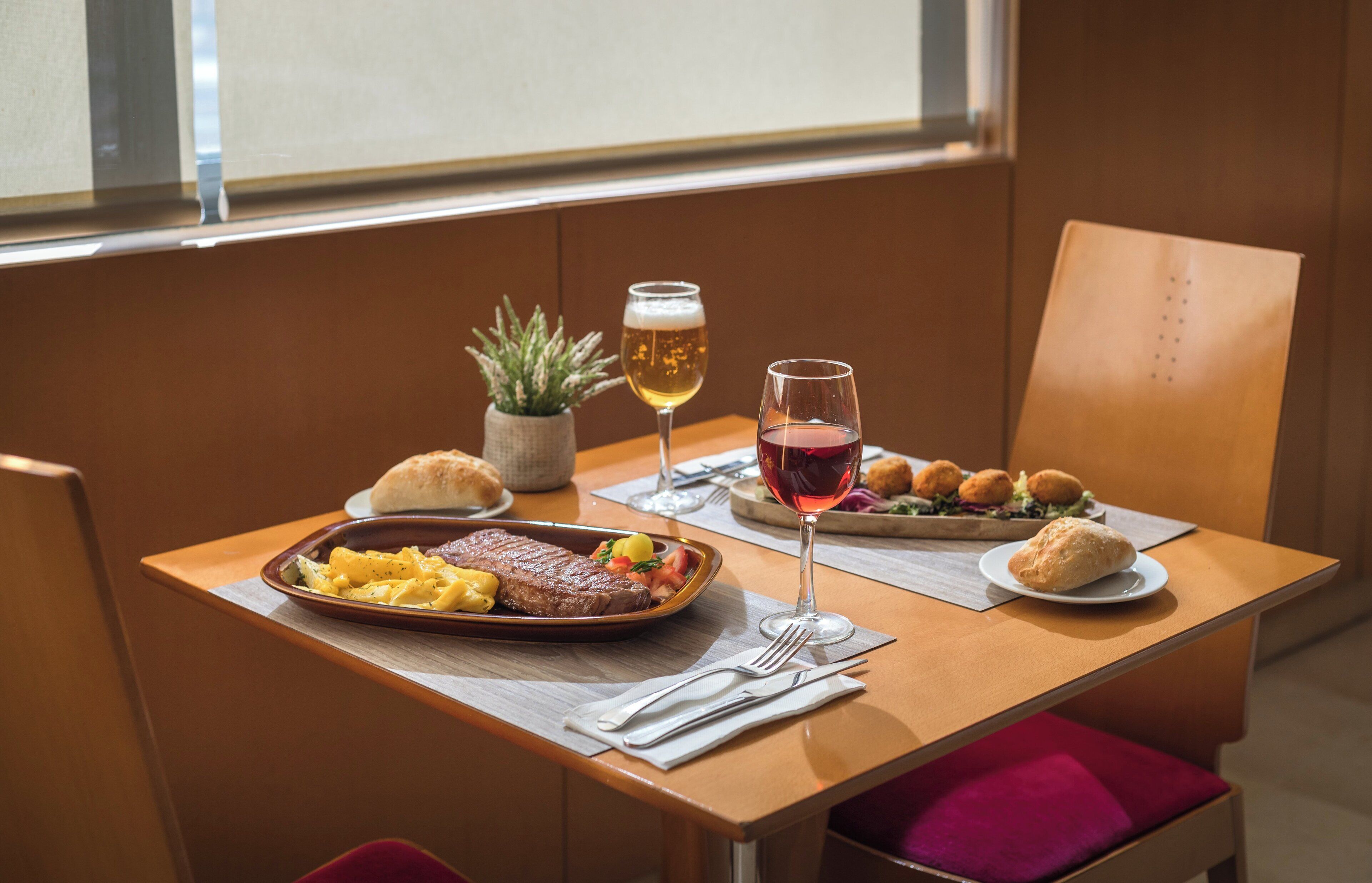 Een eettafel met een steak, pasta, brood en een glas rode wijn.