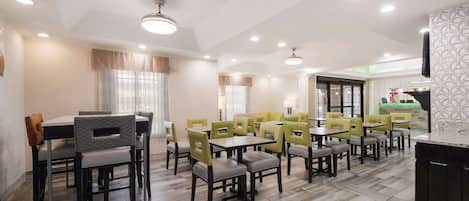 A dining area with tables and chairs, a kitchen area, and a patterned wall.
