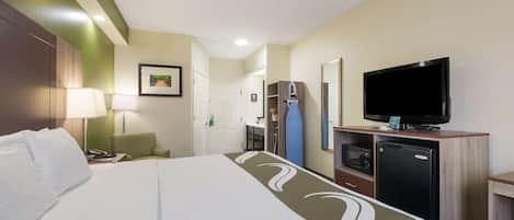 A hotel room with a bed, a desk with a lamp, a television, a microwave, and a refrigerator.
