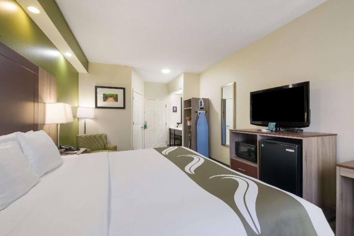 A hotel room with a bed, a television, a desk with a microwave, and a door leading to a bathroom.