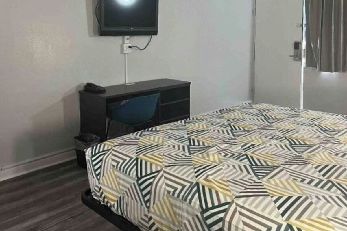 Une chambre d’hôtel équipée d’un lit, d’un bureau, d’une chaise et d’un téléviseur fixé au mur.