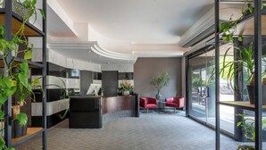 A modern reception area with a curved desk, red chairs, and potted plants. - Hotel NEWBERLIN (Berlin)