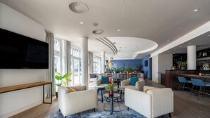 A modern hotel lobby with a seating area, a bar, and a large TV screen. - Hotel NEWBERLIN (Berlin)