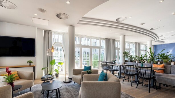 A spacious living area with a large TV, comfortable seating, and a dining area with a view of the city. - Hotel NEWBERLIN (Berlin)