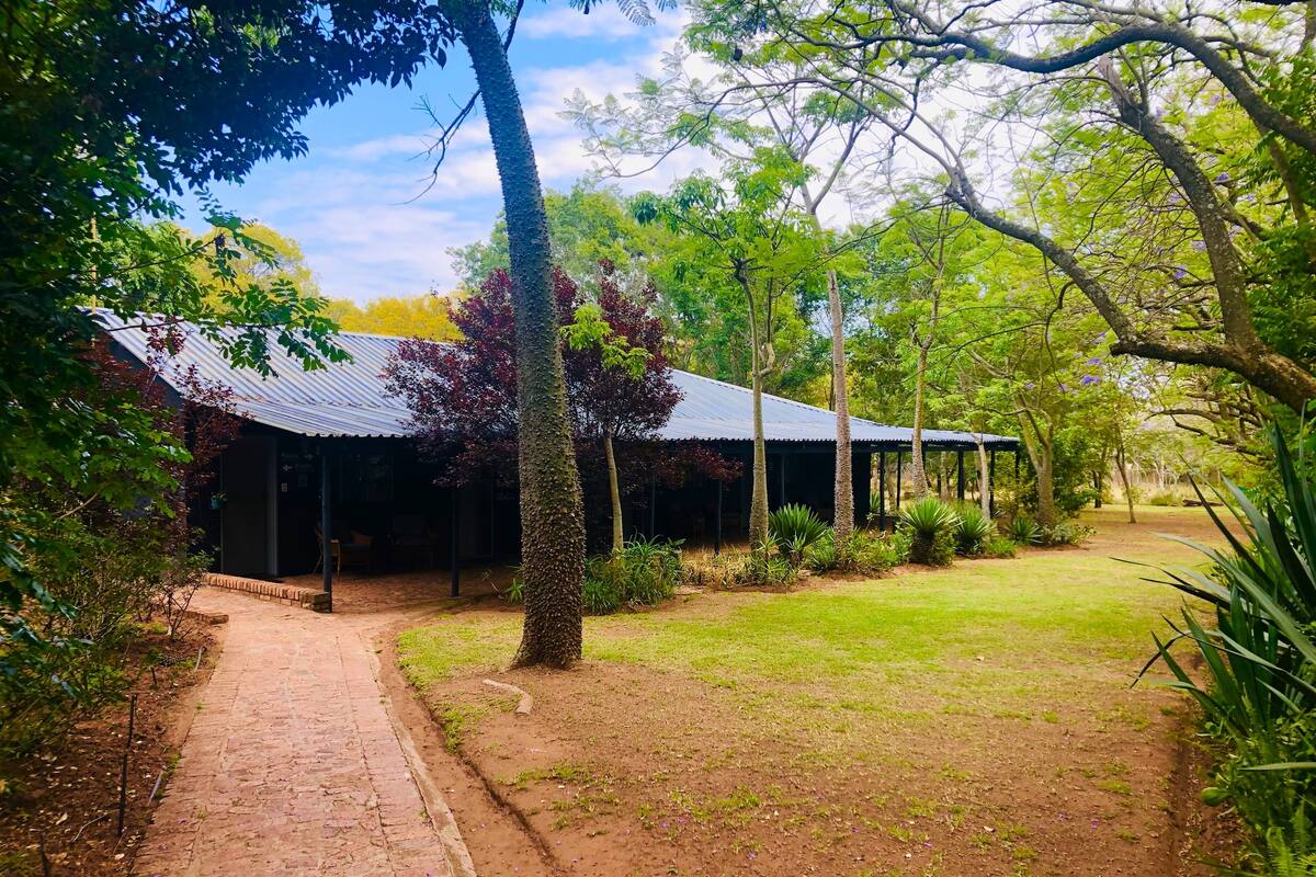 A rustic building with a corrugated metal roof, surrounded by a well-maintained garden and a paved pathway leading to the entrance.