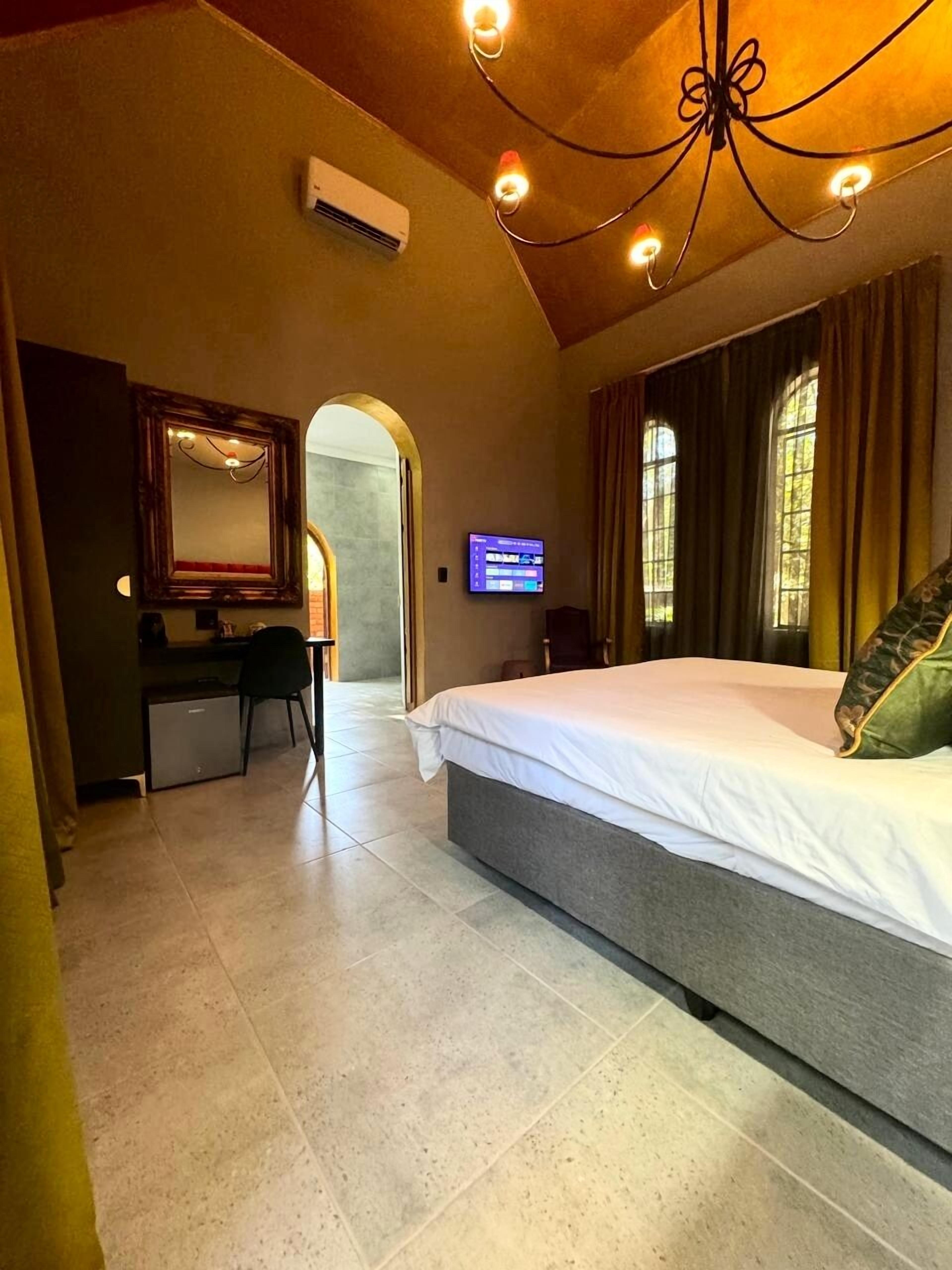 A bedroom with a large bed, a desk with a chair, a television, and a mirror.