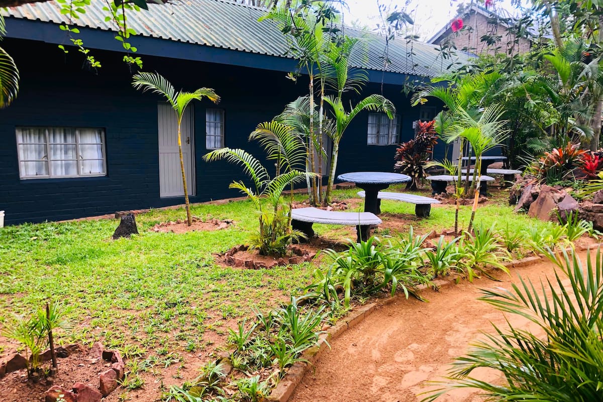 A garden with a dirt path, potted plants, and outdoor seating areas.