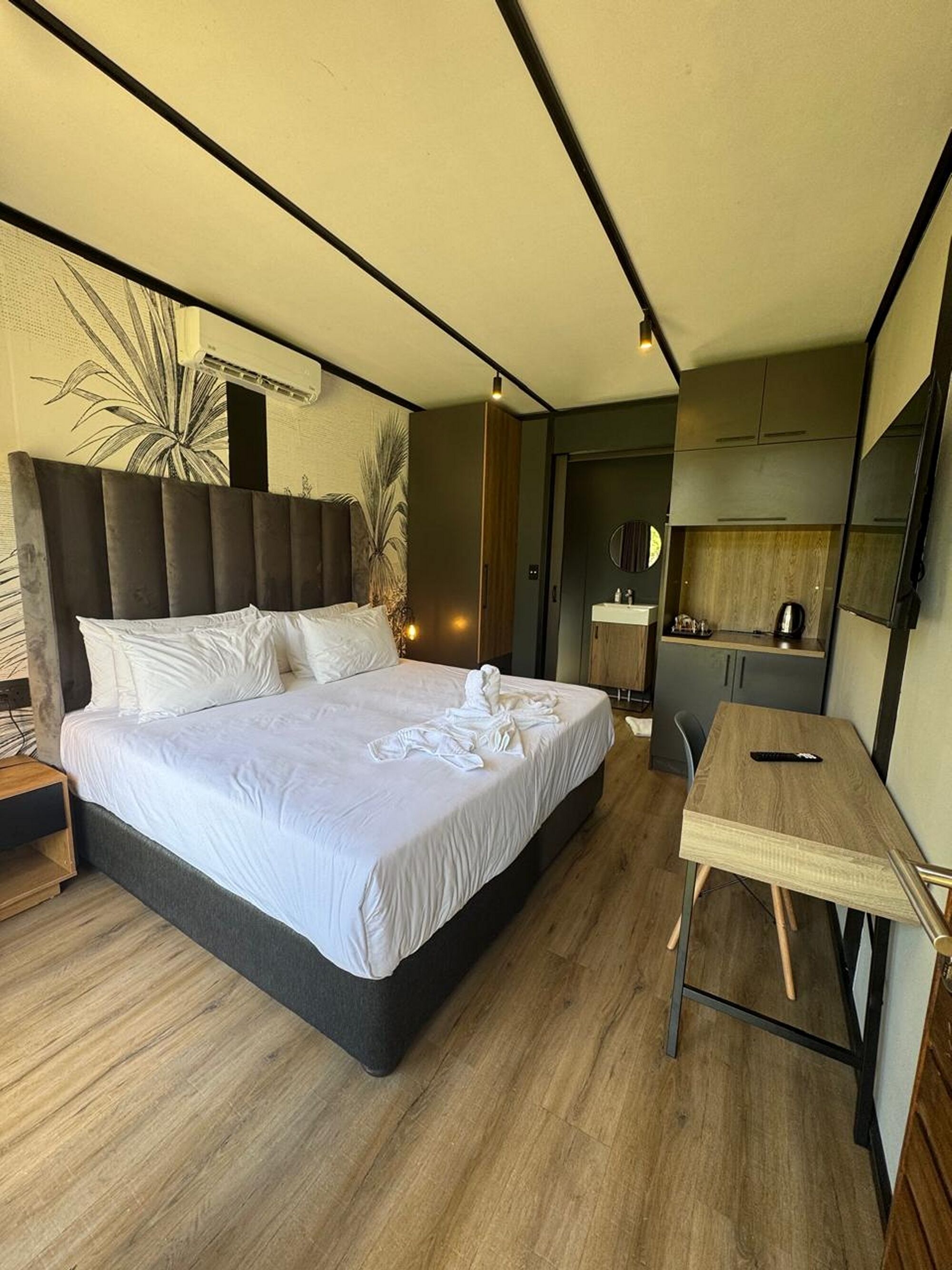 A modern hotel room with a large bed, a wooden desk, and a kitchenette.