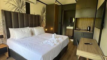 A modern hotel room with a large bed, a wooden desk, and a kitchenette.
