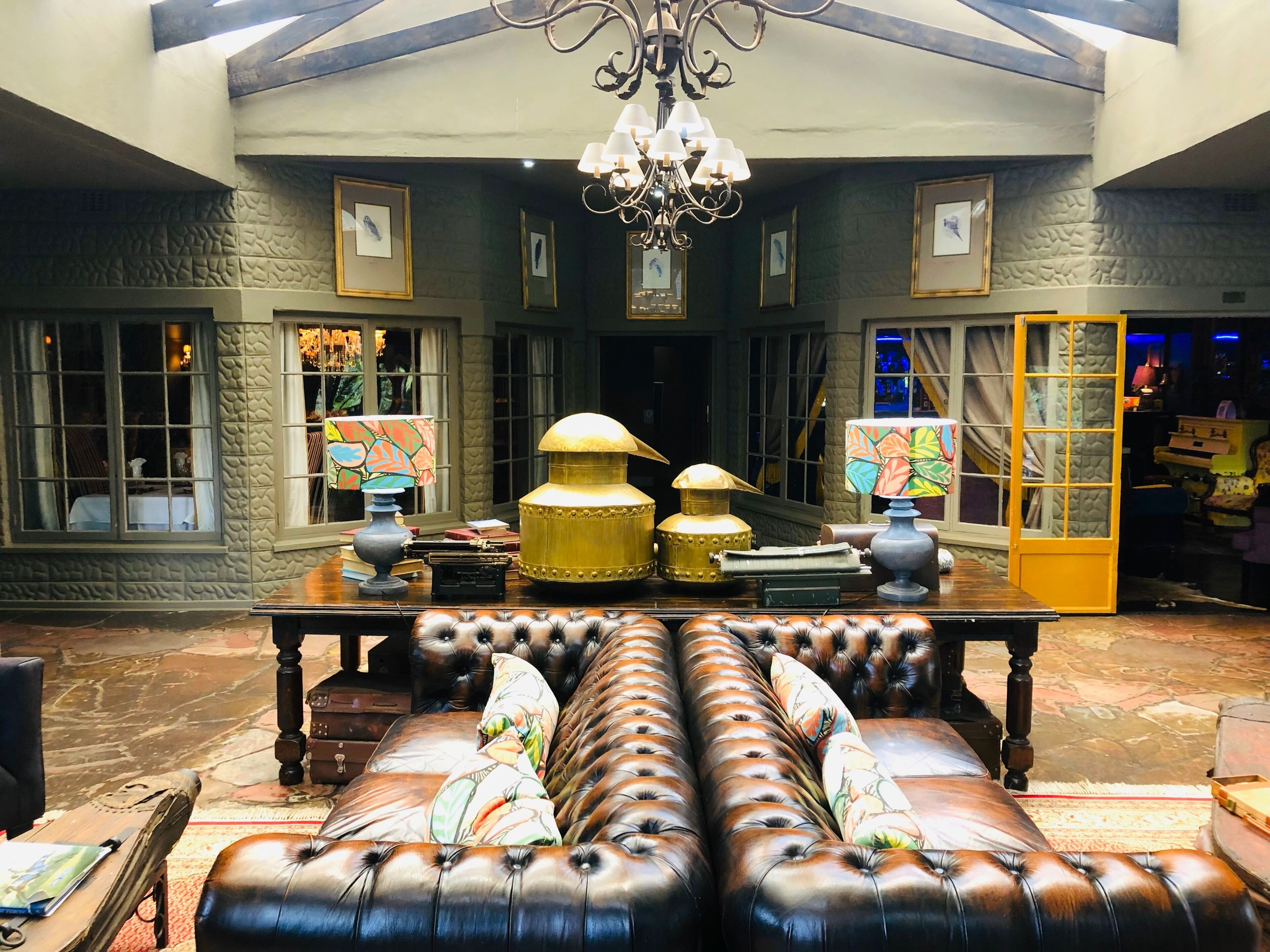 A lobby with a leather sofa, a wooden table with lamps, framed pictures on the walls, and a chandelier.