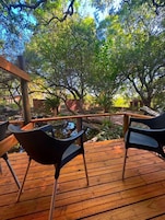 A wooden deck with two black chairs facing a pond, surrounded by lush greenery and trees.