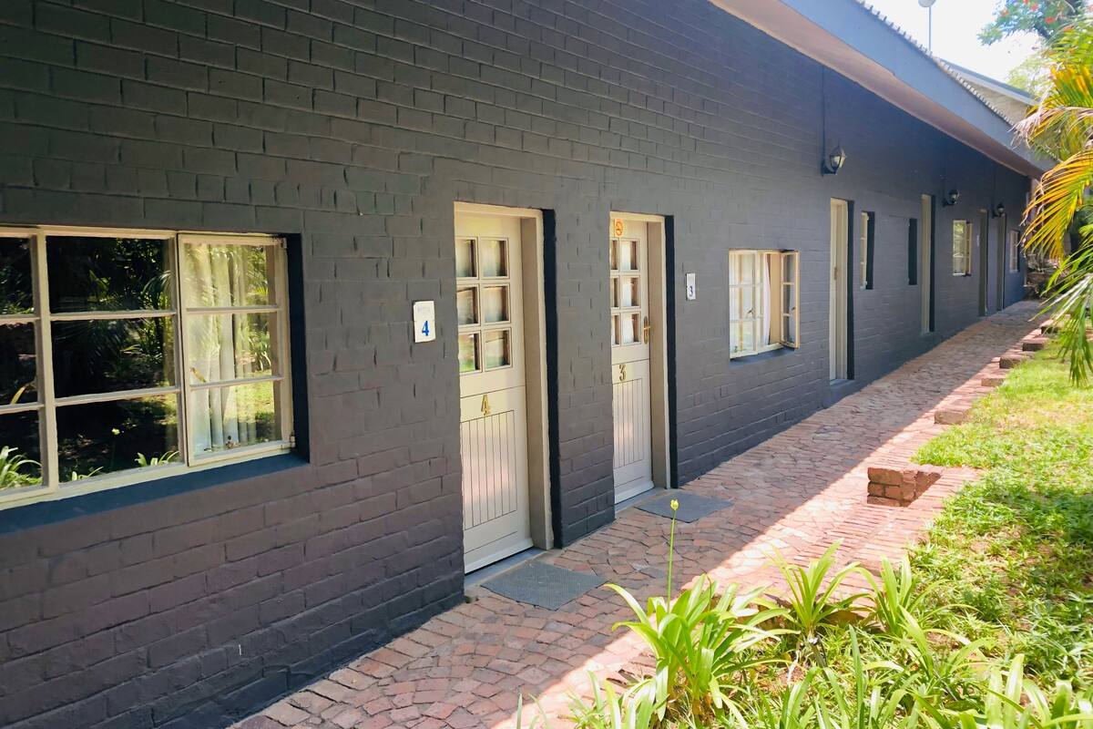 A building with a dark brick exterior, numbered doors, and windows with curtains.