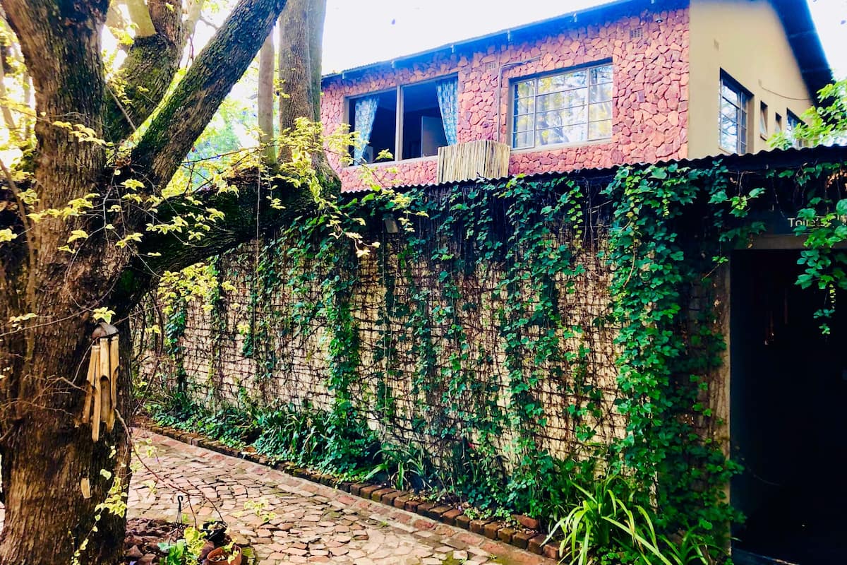 A stone building with a pink roof, partially covered in ivy, and a cobblestone pathway leading to a door.