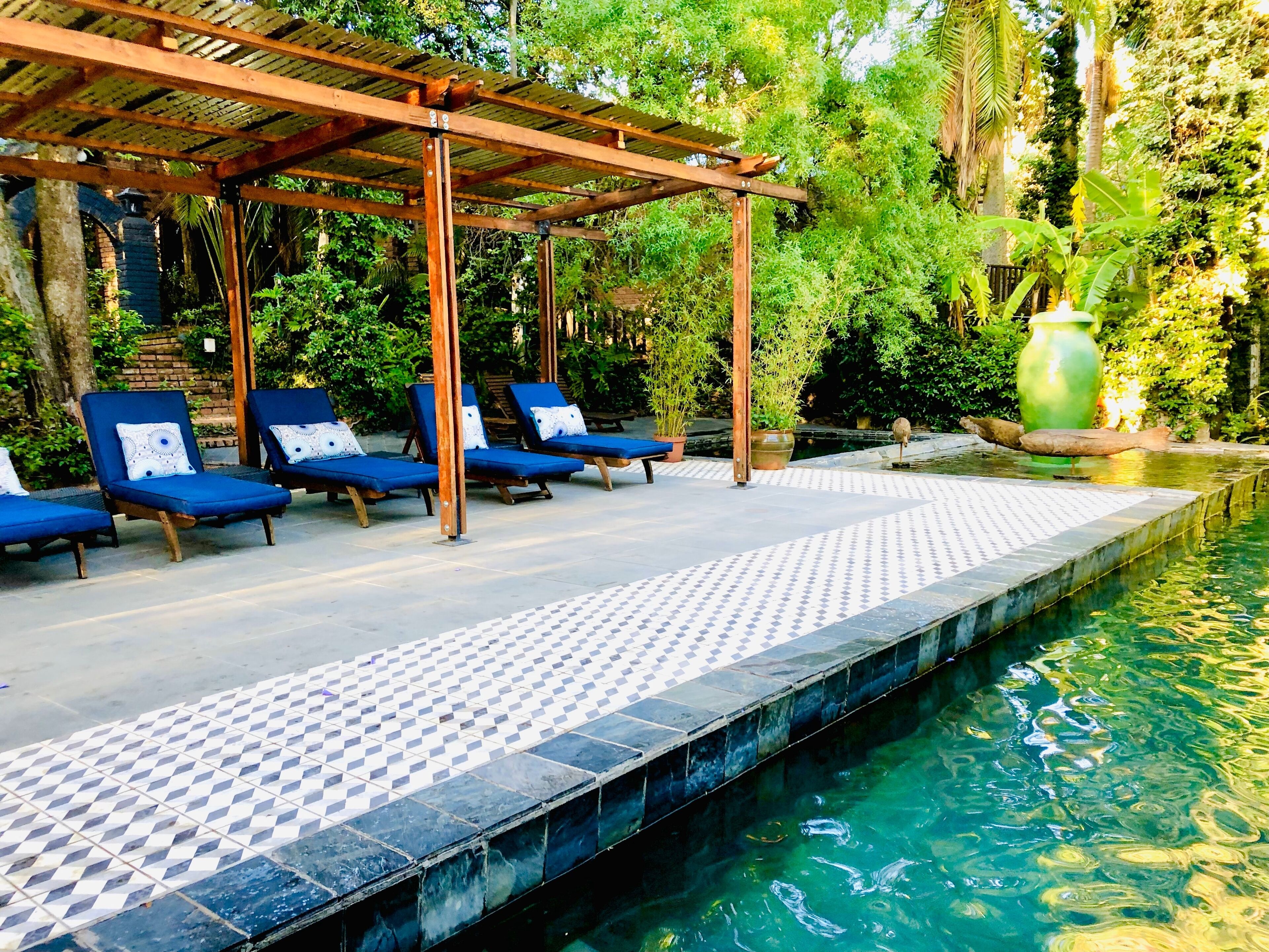 A poolside area with lounge chairs, a pergola, and a tiled walkway leading to the pool.