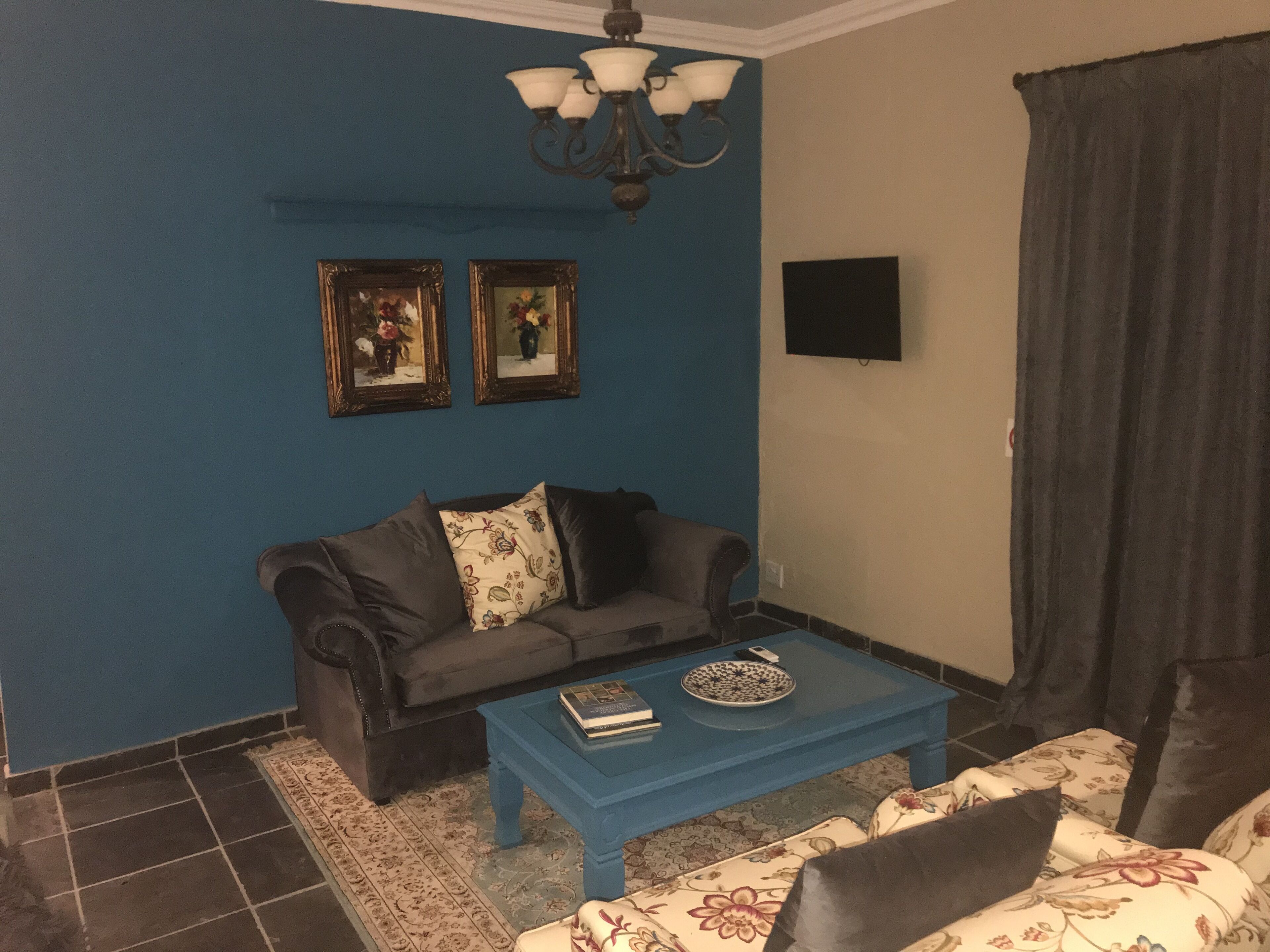 A living room with a blue wall, a dark sofa, a blue coffee table, and a patterned sofa.