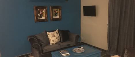 A living room with a blue wall, a dark sofa, a blue coffee table, and a patterned sofa.