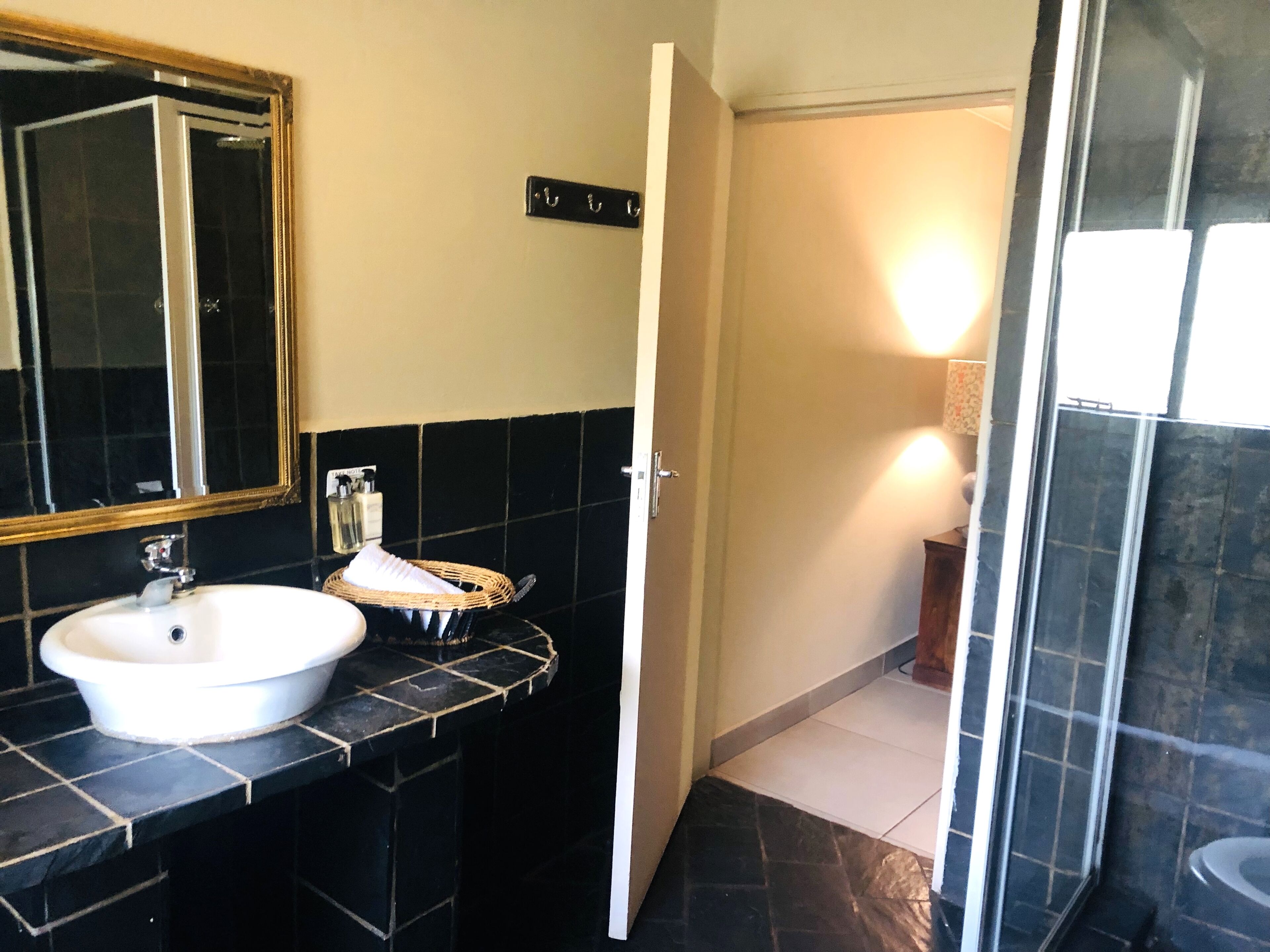 A bathroom with a white sink, a mirror, black tiles, a wicker basket, and a shower area.