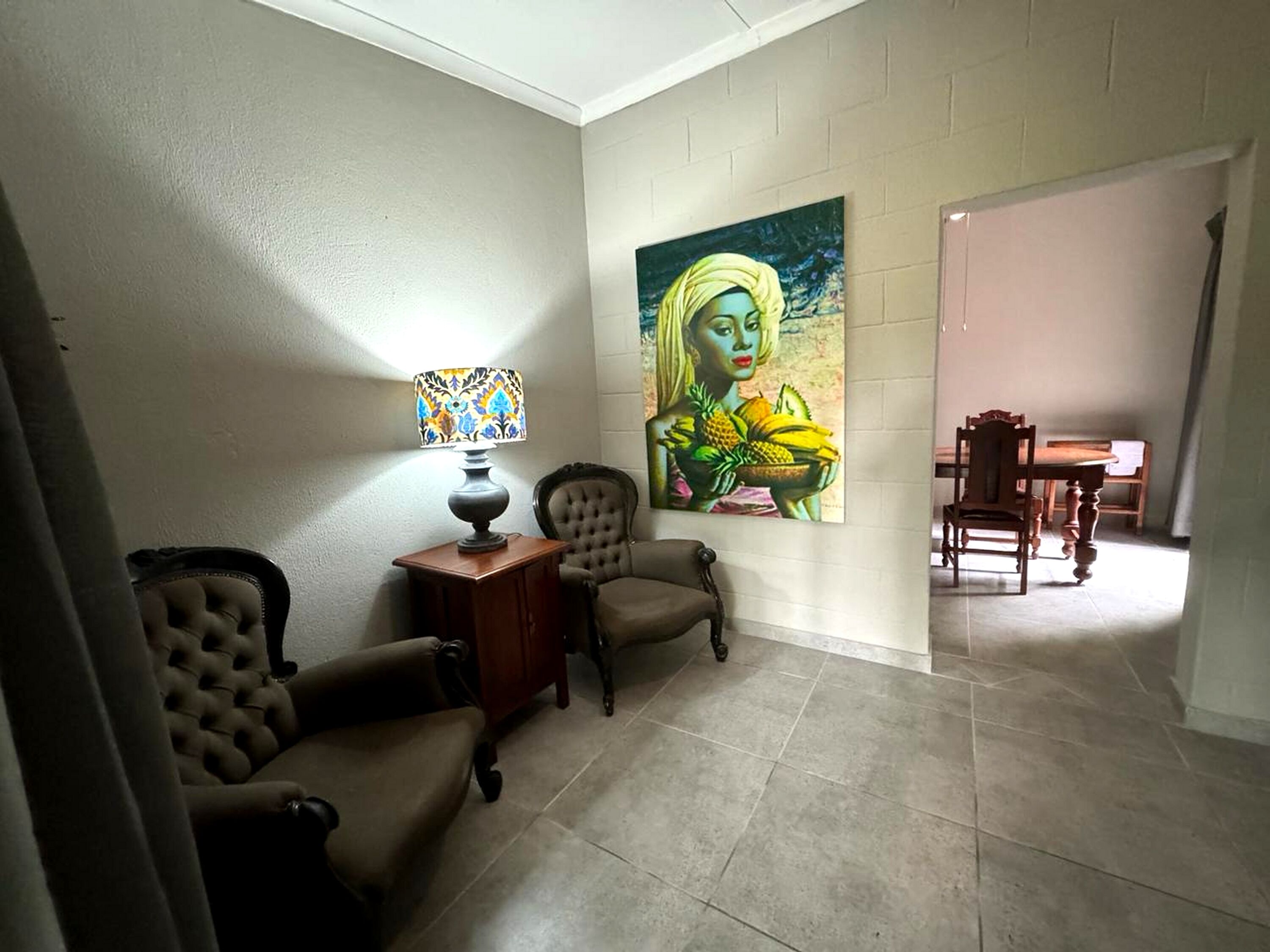 A living room with a sofa, armchairs, a table with a lamp, and a painting on the wall.