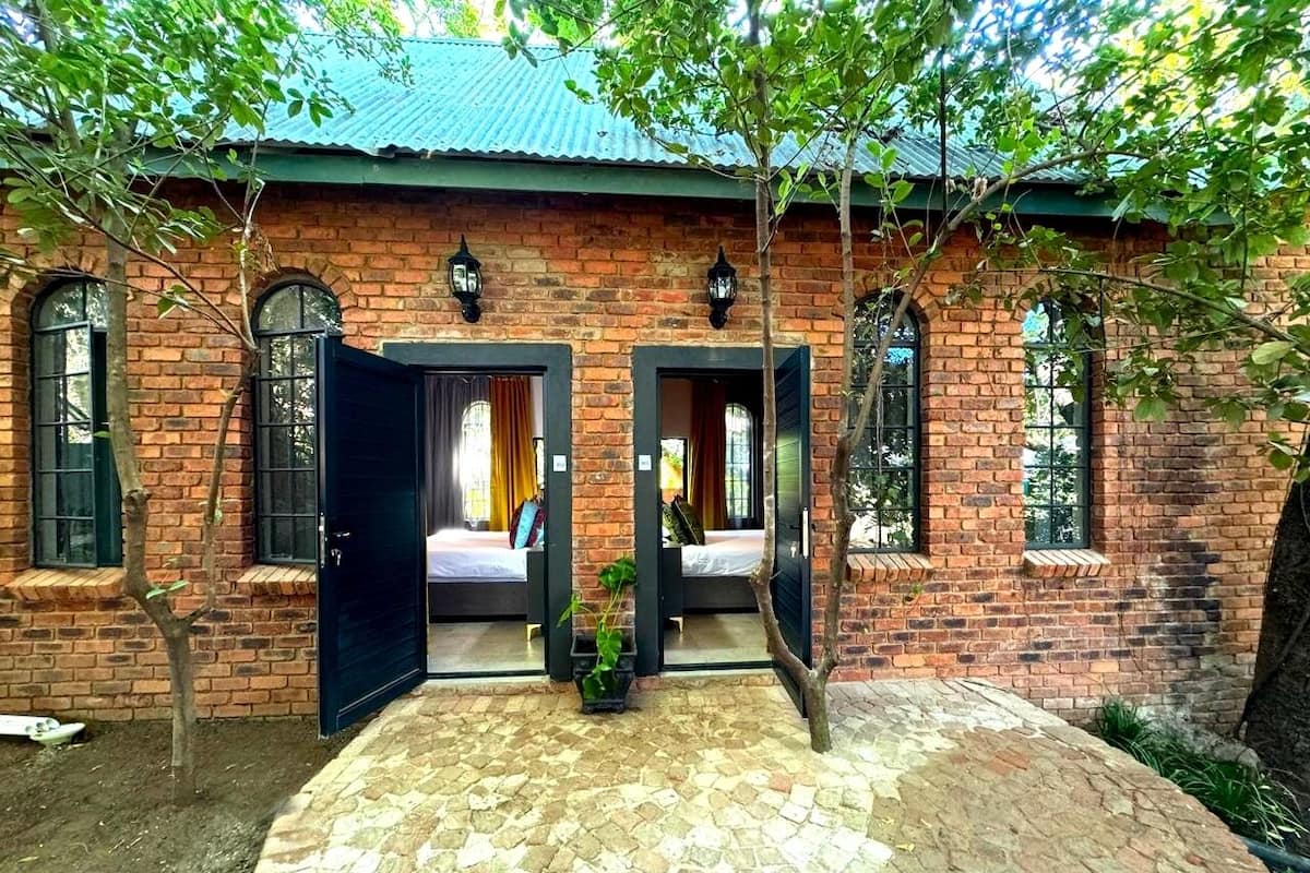 A brick building with two open doors leading to rooms with beds and windows.
