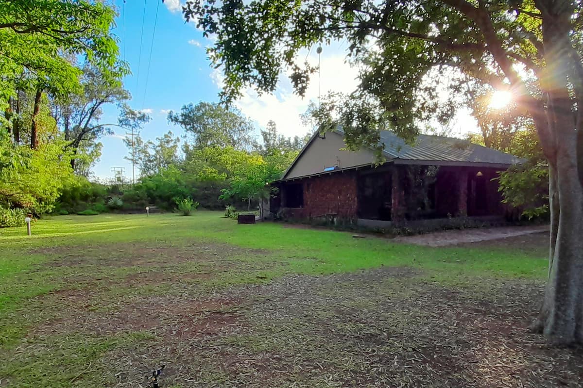 A grassy area with a rustic building, surrounded by trees and a clear sky.